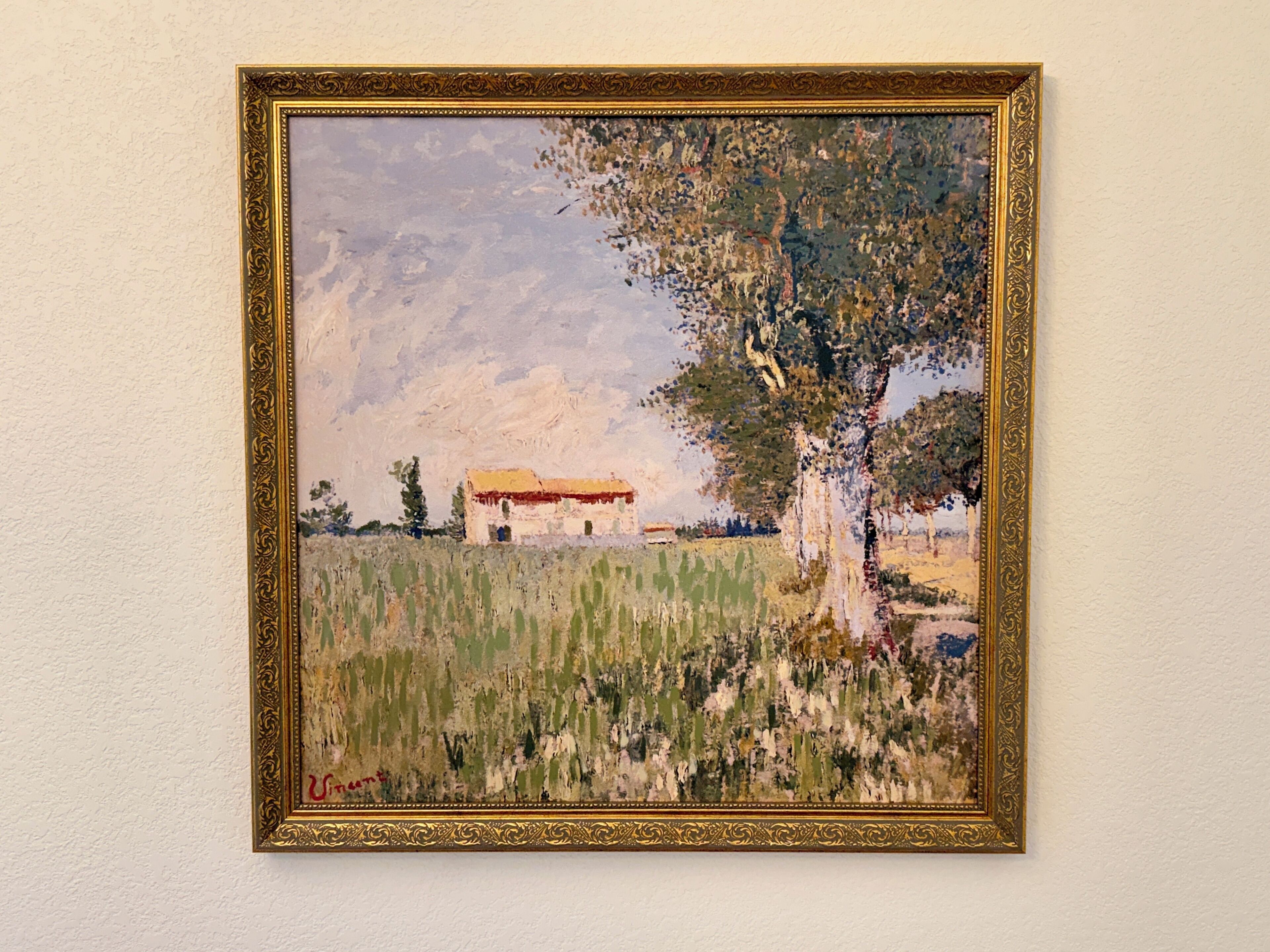 A framed painting of a landscape with a tree and a building.