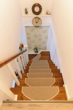 A wooden staircase with carpeted steps leading to a landing with a floral wallpaper backdrop.