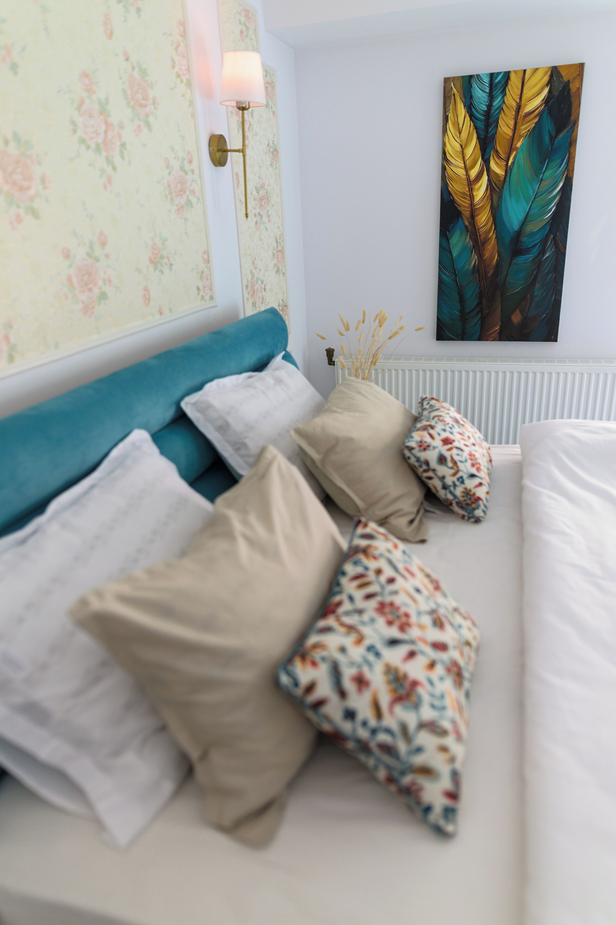 A bedroom with a bed, pillows, a wall-mounted lamp, and a painting.