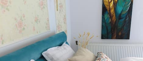 A bedroom with a bed, pillows, a wall-mounted lamp, and a painting.