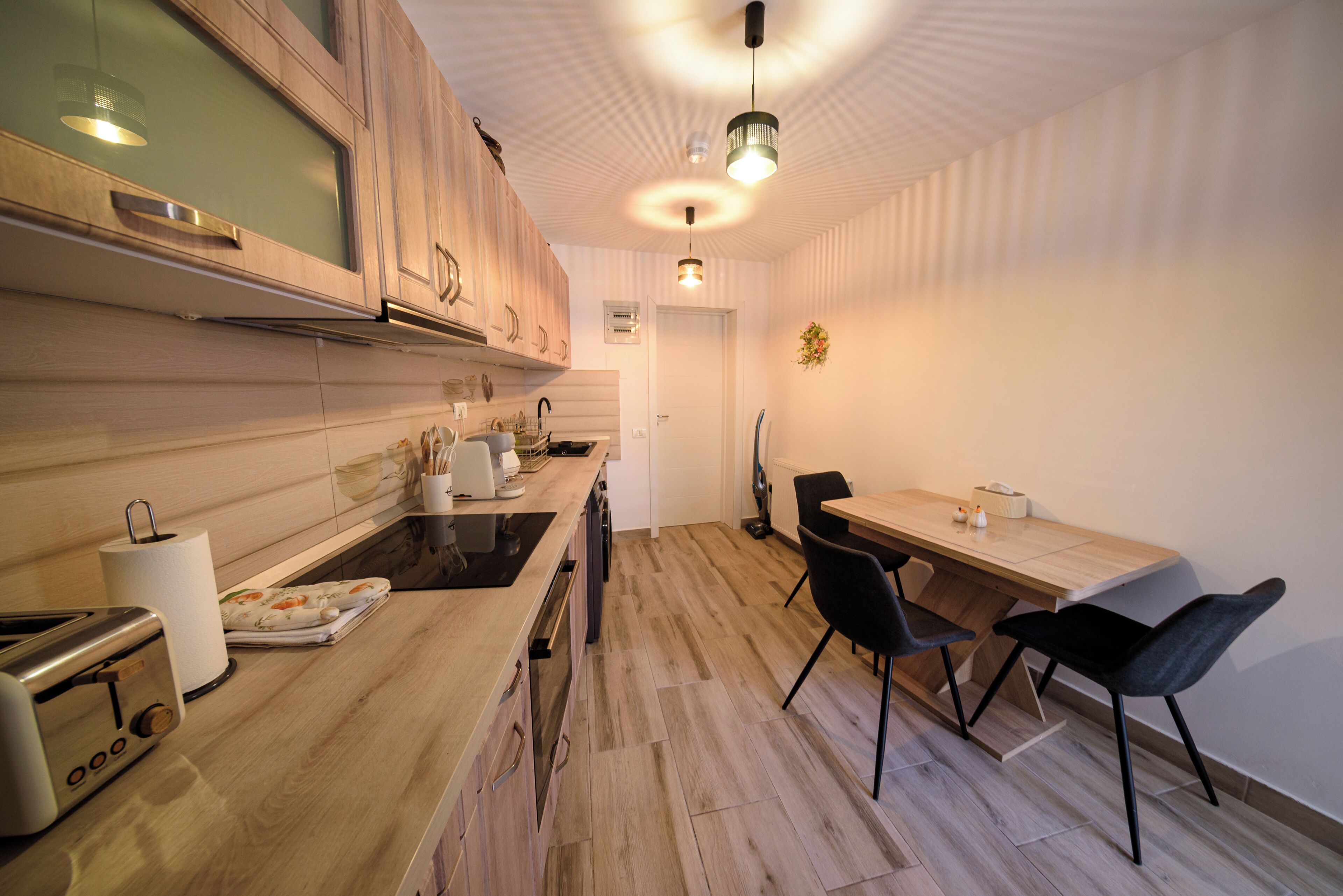A modern kitchen with wooden cabinets, a built-in oven, and a dining area with a table and chairs.