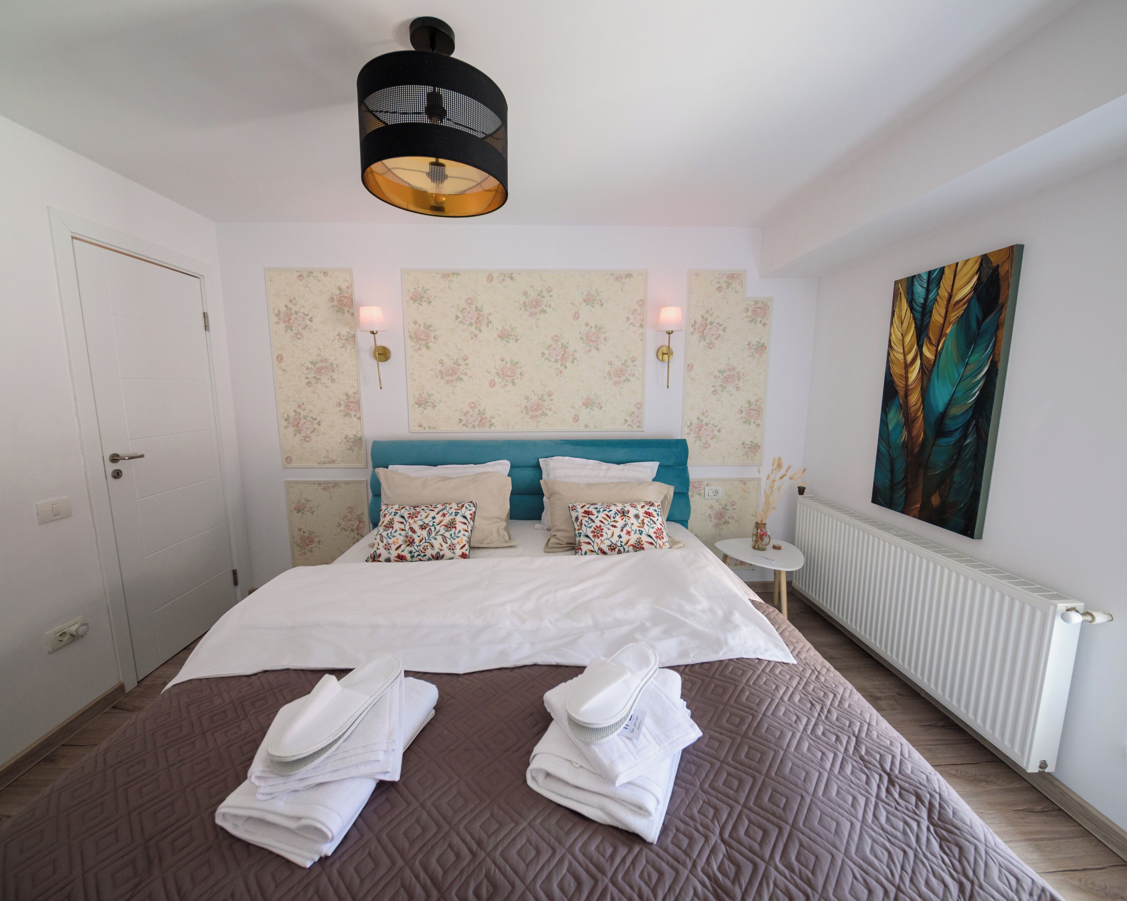 Une chambre d’hôtel avec un lit, deux lampes fixées au mur, un radiateur et un grand tableau.