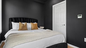 Una camera da letto con un letto, un comodino, una porta bianca e un termostato a parete.