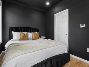A bedroom with a bed, a bedside table, a white door, and a thermostat on the wall. - 2 Mins from King St < > A Boutique Old Town Xcape (Alexandria)