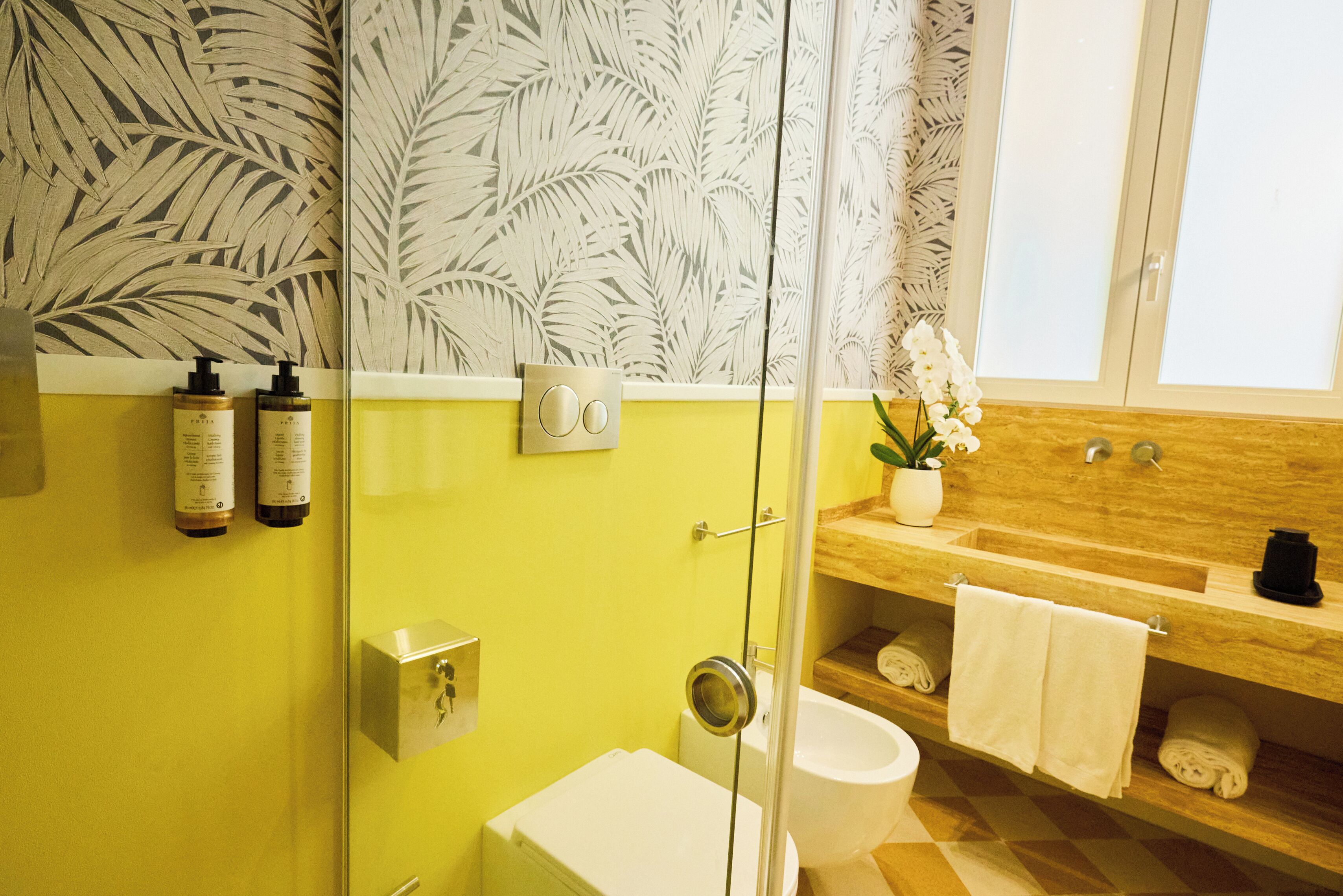 A bathroom with a glass shower enclosure, a white toilet, a wooden vanity with a sink, and a potted orchid.