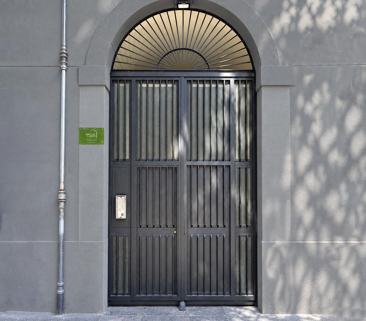 A large, dark metal gate with vertical bars, a green sign, and a light fixture above it.