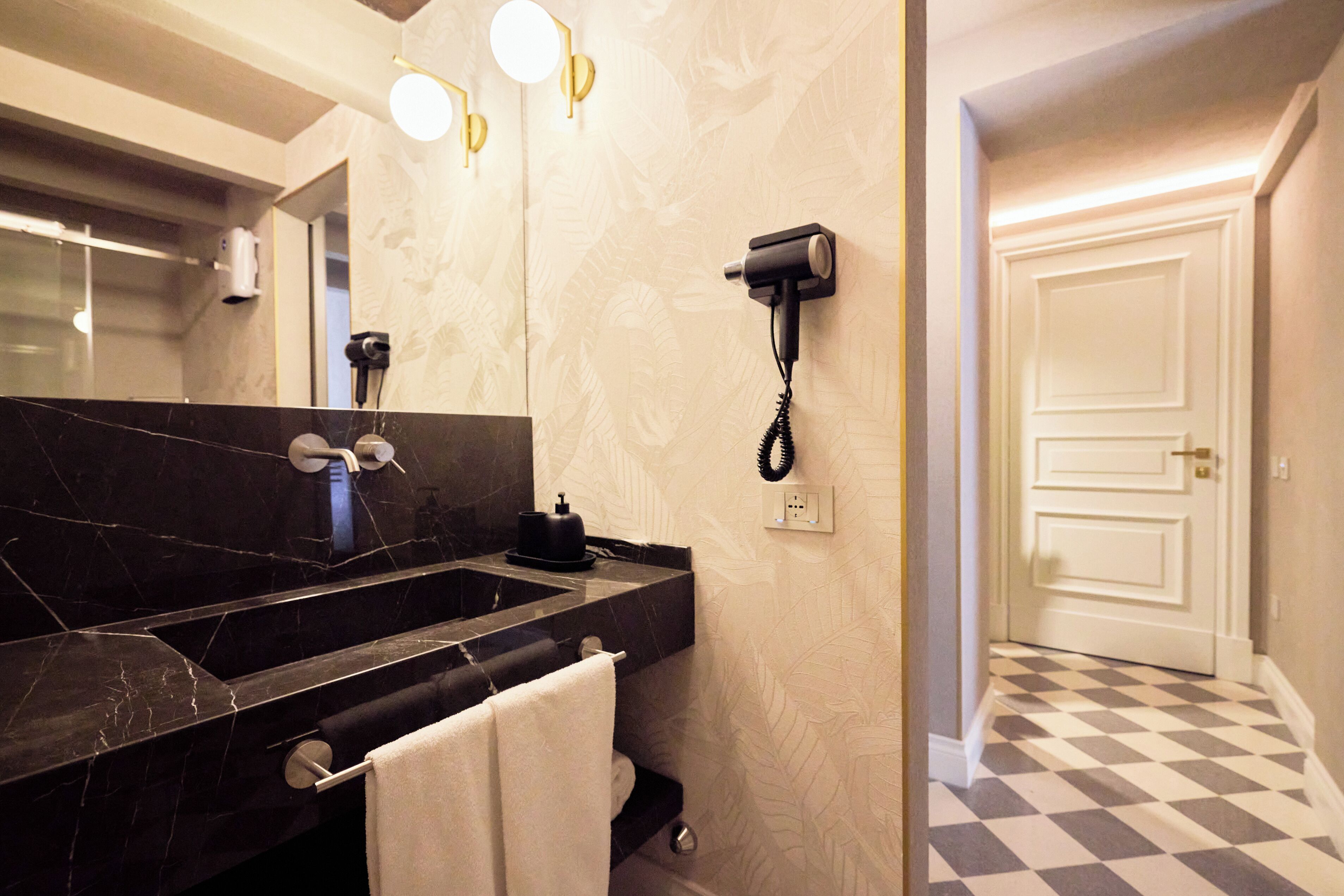 Une salle de bain avec un lavabo en marbre noir, un porte-serviettes et un sèche-cheveux fixé au mur.