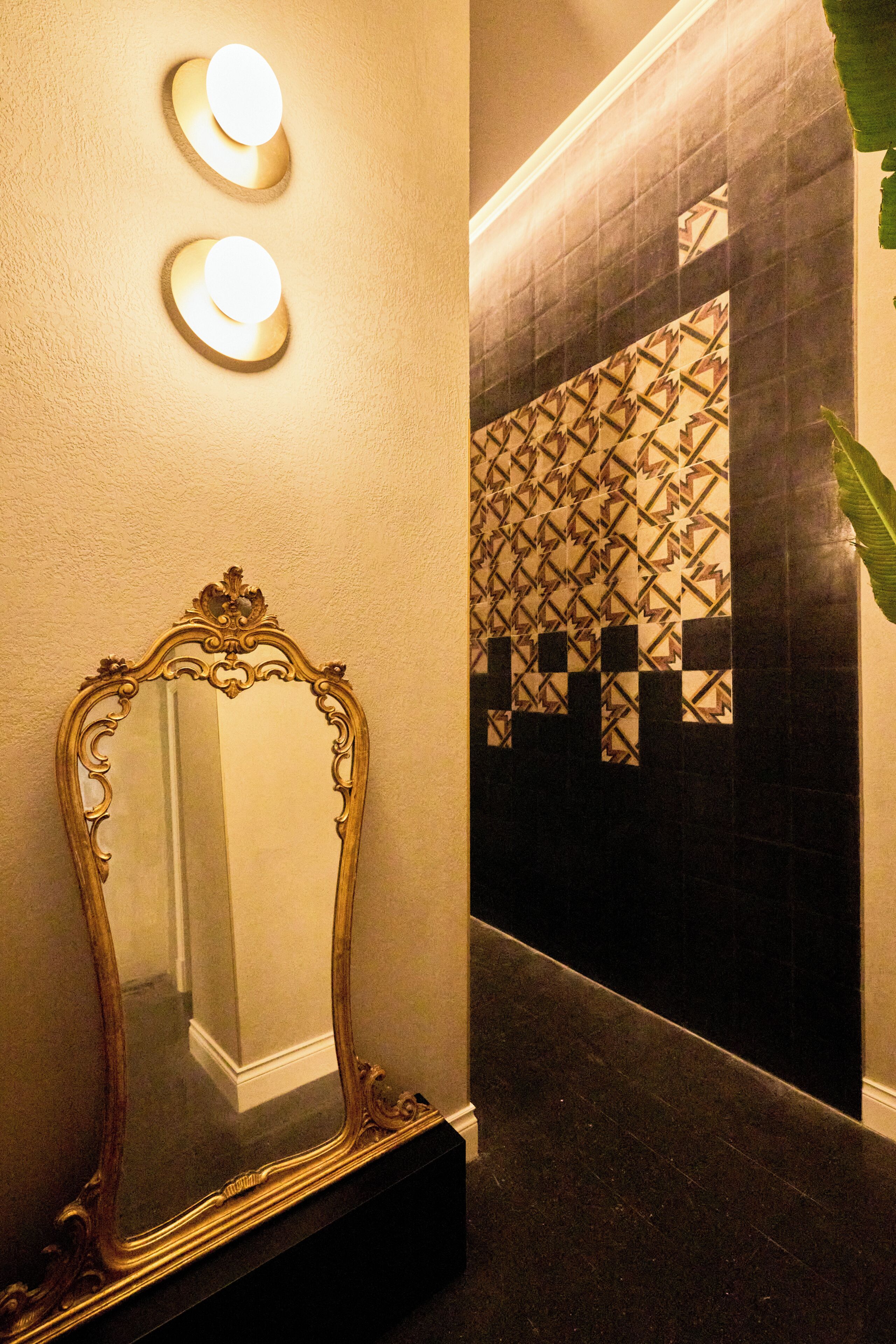 A mirror with an ornate frame, a wall-mounted light fixture, and a patterned wall.