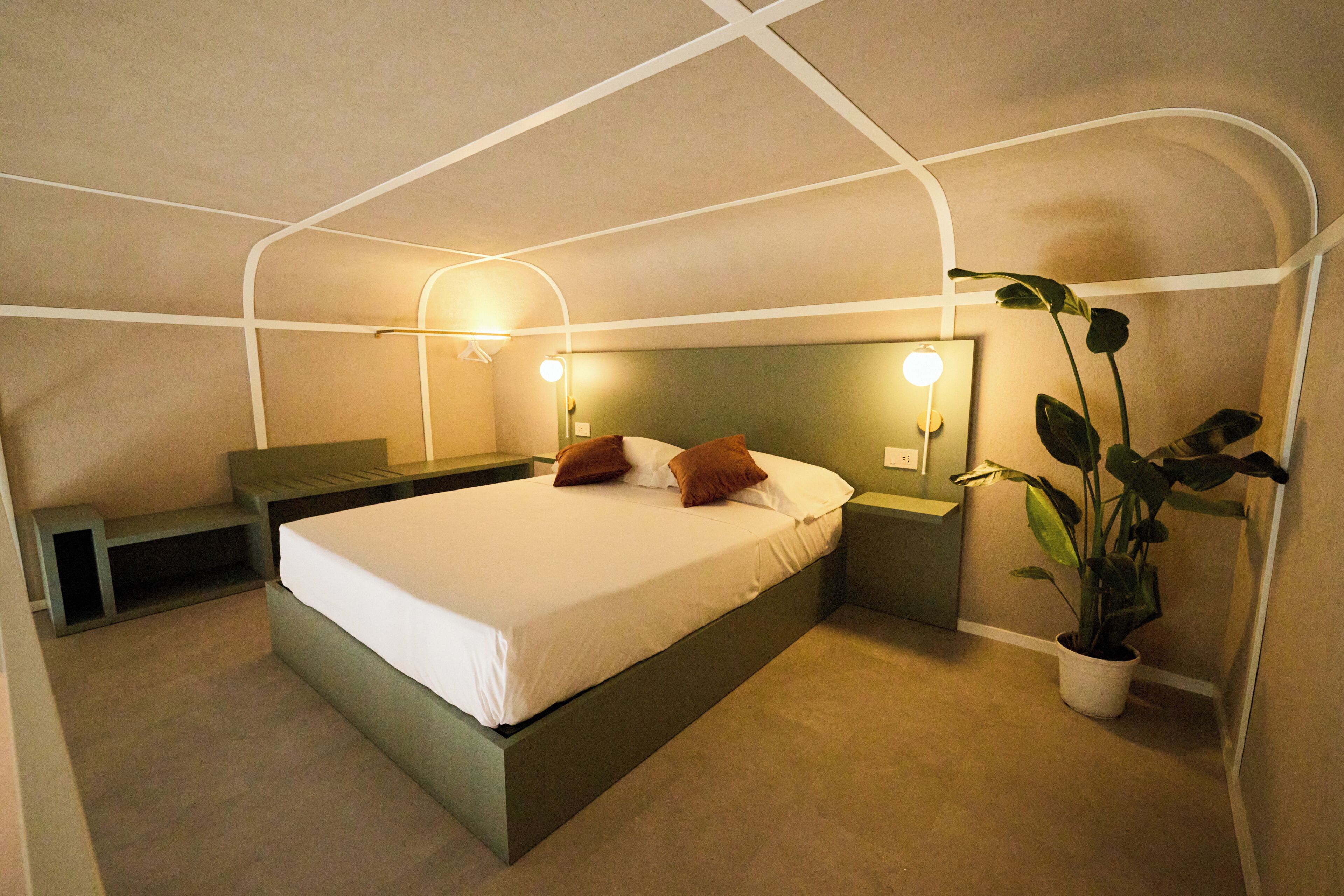 A modern bedroom with a bed, bedside tables, a nightstand, a hanging light fixture, and a potted plant.