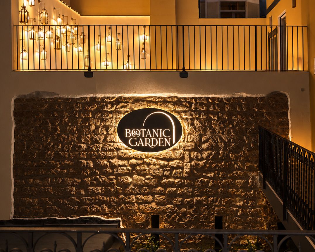 A stone wall with a sign for 'Botanic Garden' illuminated by warm lighting.