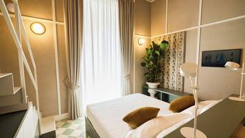 A hotel room with a bed, a desk, a lamp, a plant, and a painting on the wall.