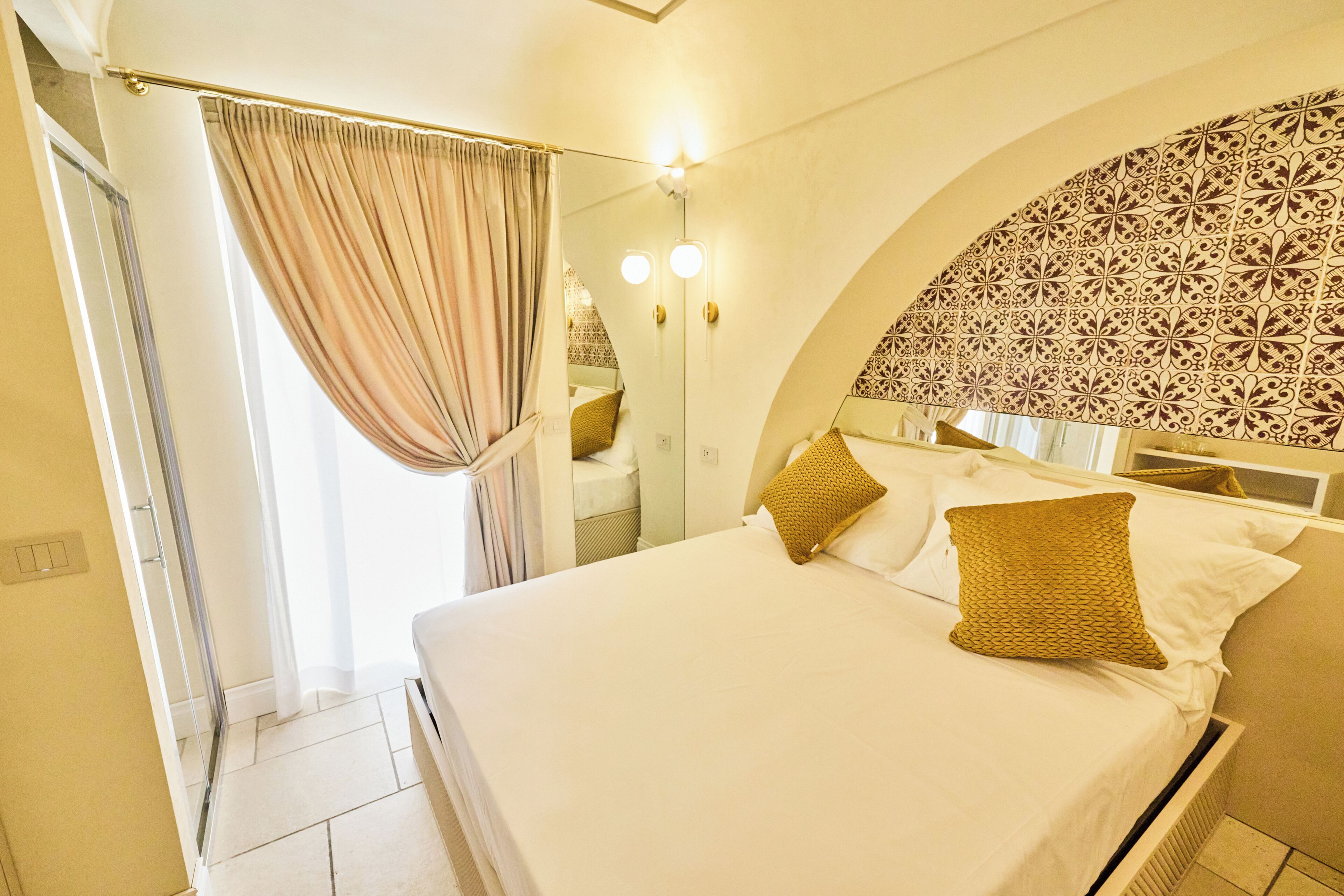 Quarto de hotel com uma cama, cortinas, chuveiro e uma parede com padrão decorativo.