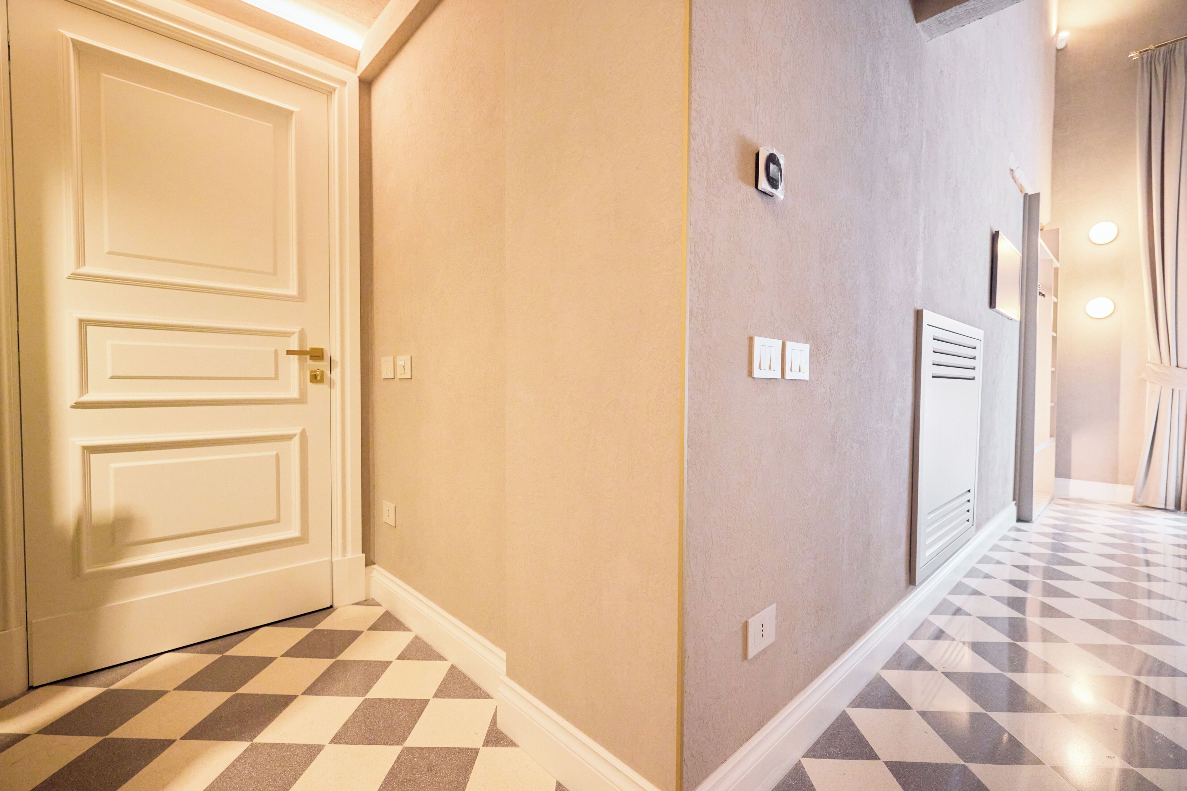 A hallway with a checkered floor, a white door, and a wall with a thermostat and light switch.