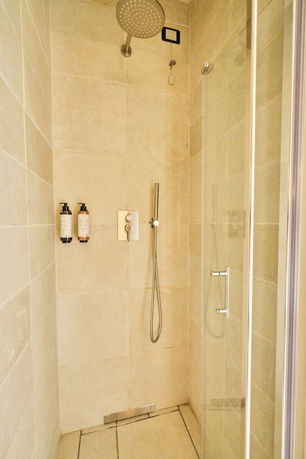 A modern shower area with a handheld showerhead, a wall-mounted control panel, and two bottles of shampoo and conditioner. - botanic garden (Naples)