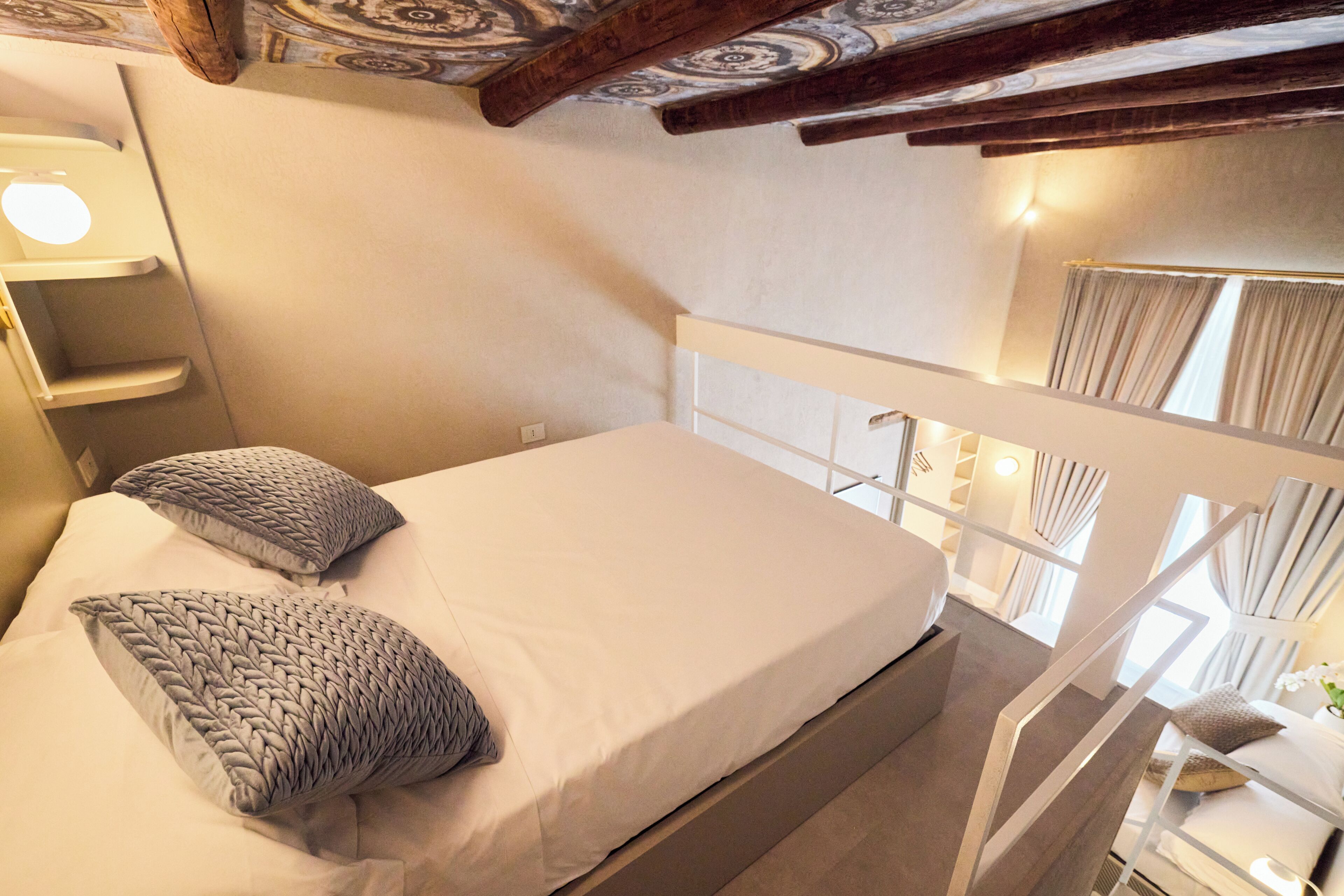 Une chambre à coucher avec un lit, des oreillers, une table de chevet, une lampe et une vue sur l’extérieur.
