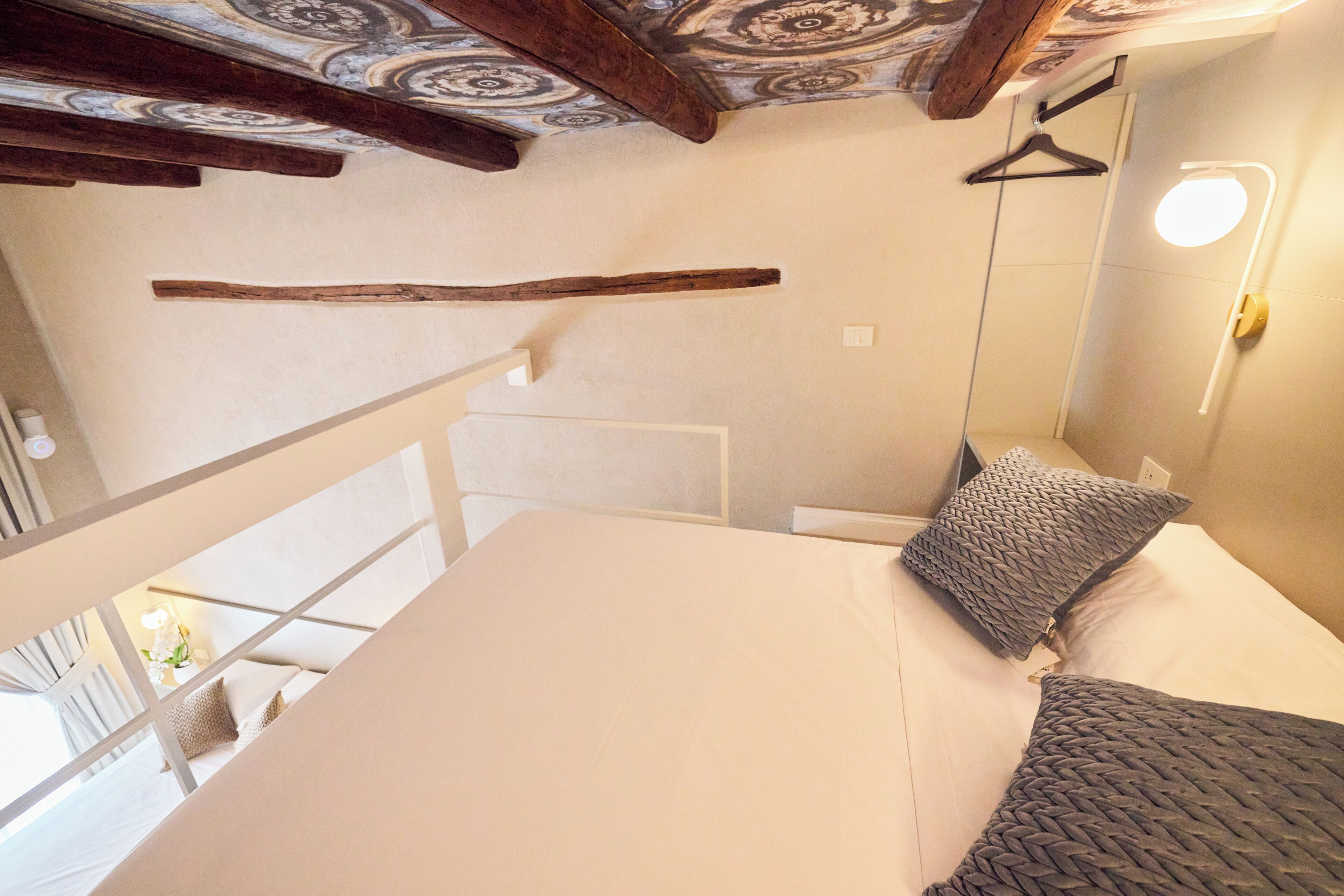 A bedroom with a bed, a hanging light fixture, and a wooden beam ceiling.
