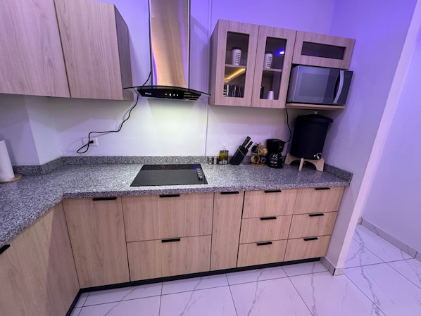 A kitchen with a granite countertop, wooden cabinets, a built-in microwave, and various kitchen utensils.