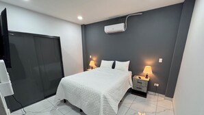 A hotel room with a bed, bedside lamps, a TV, and a wall-mounted air conditioner.