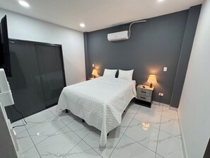 Habitación de hotel con cama, lámparas de noche, televisor y aire acondicionado instalado en la pared.