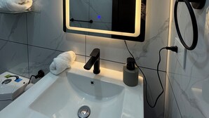 A bathroom with a white sink, a mirror with a light, a towel on the wall, and a black faucet.