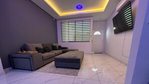A modern living room with a sectional sofa, a flat-screen TV mounted on the wall, and a ceiling with recessed lighting.