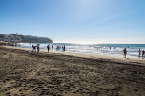 A beach with footprints, a clear sky, and buildings in the background. - Sun & Figs (San Bartolomé de Tirajana)