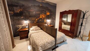 Een slaapkamer met een bed, een houten dressoir, een grote spiegel en een muurschildering van een stadsgezicht.