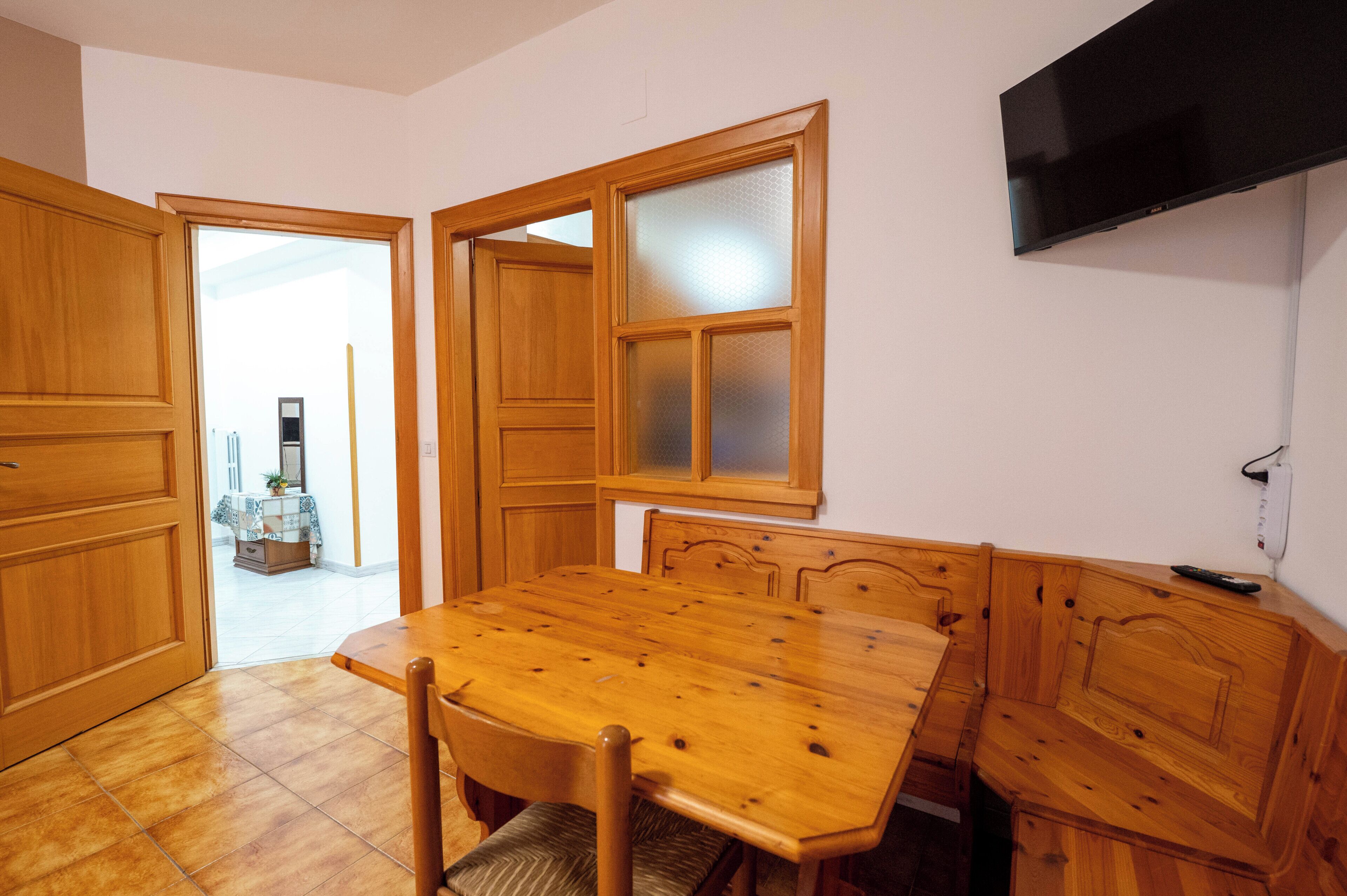 Una mesa de comedor de madera con sillas, un banco y un televisor montado en la pared.