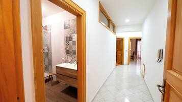 Un couloir d’hôtel avec un cadre de porte en bois, une salle de bain avec une douche et un lavabo, et un sol carrelé.
