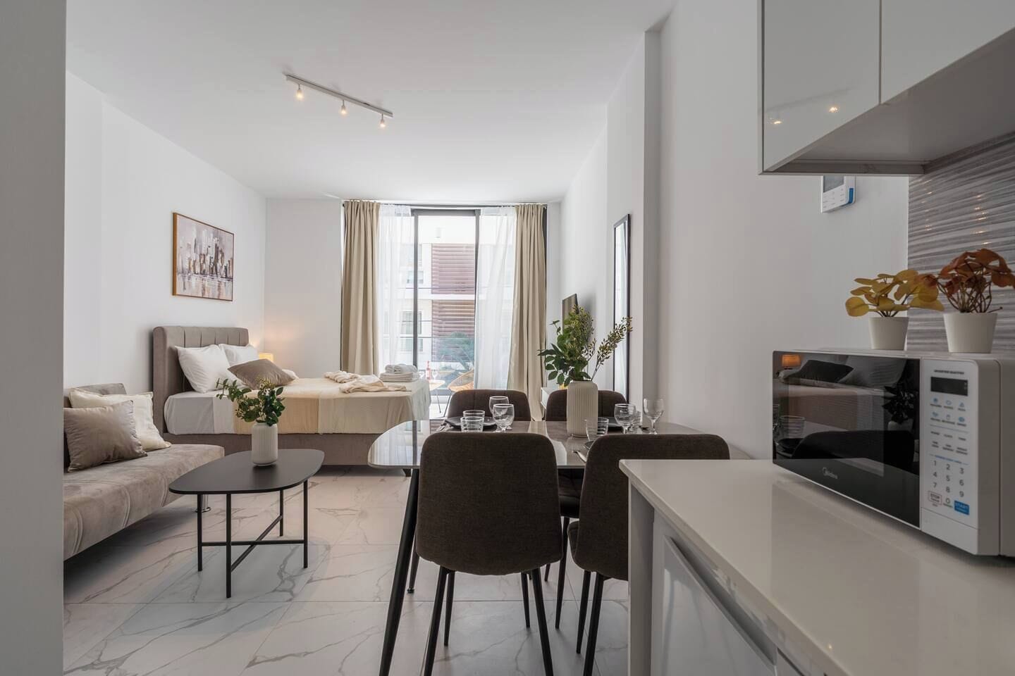 A modern apartment with a dining area, a sofa, a bed, and a kitchen.