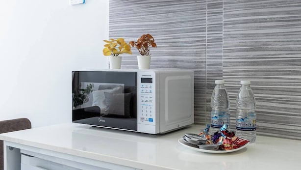 A modern kitchen with a white microwave, a small potted plant, and a tray with snacks and bottled water. - Opal Signature Studio (Larnaca)