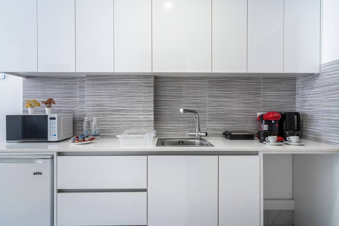 A modern kitchen with white cabinets, a stainless steel sink, a microwave, a coffee maker, and a dish rack.