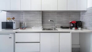 A modern kitchen with white cabinets, a stainless steel sink, a microwave, a coffee maker, and a dish rack. - Opal Signature Studio (Larnaca)