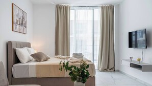 Quarto de hotel moderno com cama, televisão, planta e janela com cortinas.