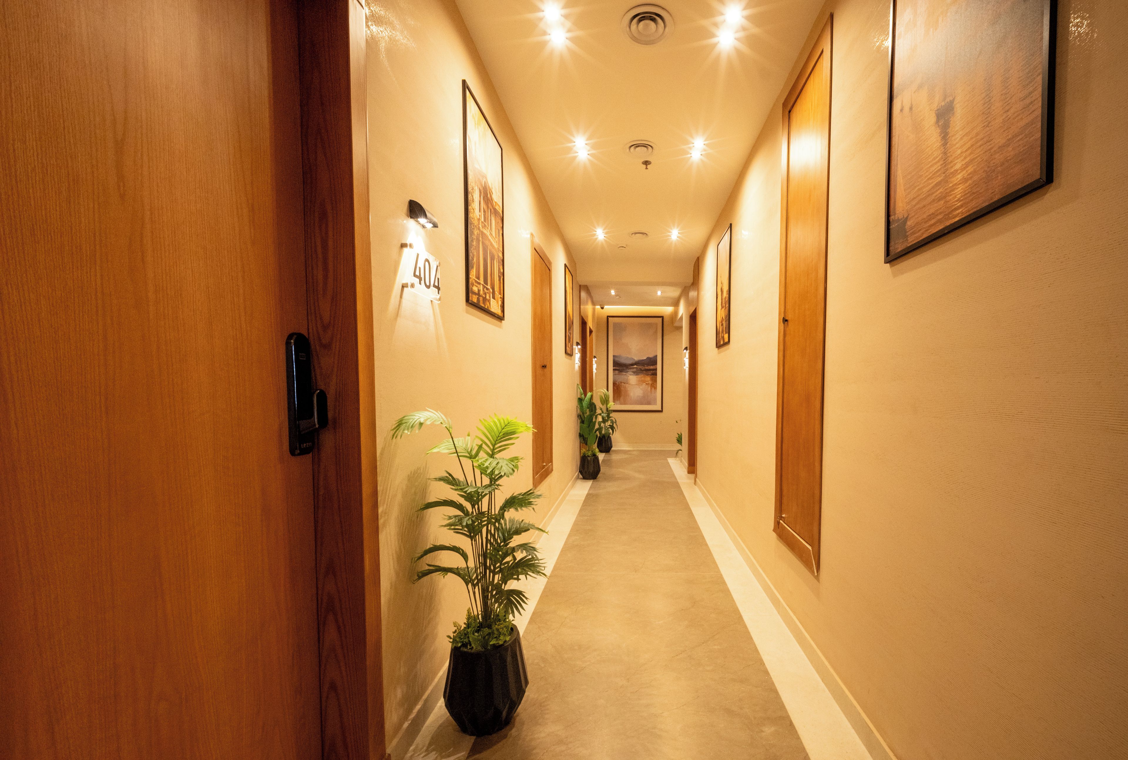 Corredor de hotel com portas de madeira, quadros nas paredes e plantas em vasos.