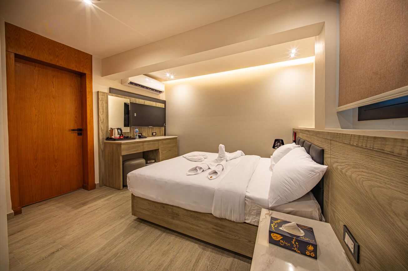 Habitación de hotel con una cama de madera, un escritorio con computadora, un espejo y un televisor.
