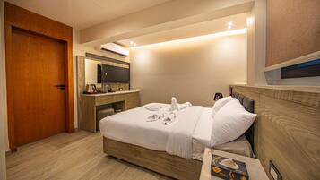 Habitación de hotel con una cama de madera, un escritorio con computadora, un espejo y un televisor.