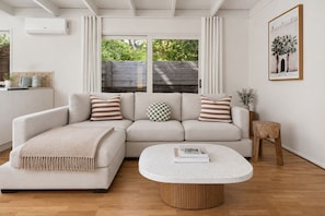 A living room with a beige sectional sofa, a round coffee table, a wooden stool, and a framed picture on the wall. - Moonbay by Ready Set Stay (Rye)