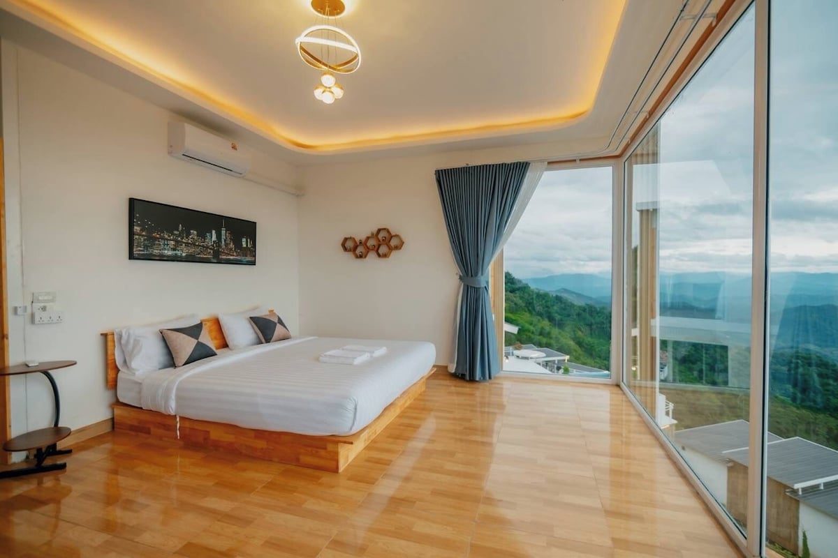 A modern bedroom with a large bed, a cityscape painting, a view of mountains, and a large window.