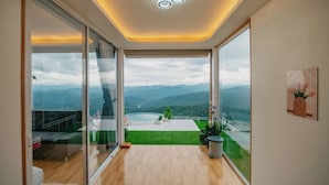 Un intérieur moderne avec une grande porte-fenêtre coulissante donnant sur un balcon avec vue sur les montagnes.
