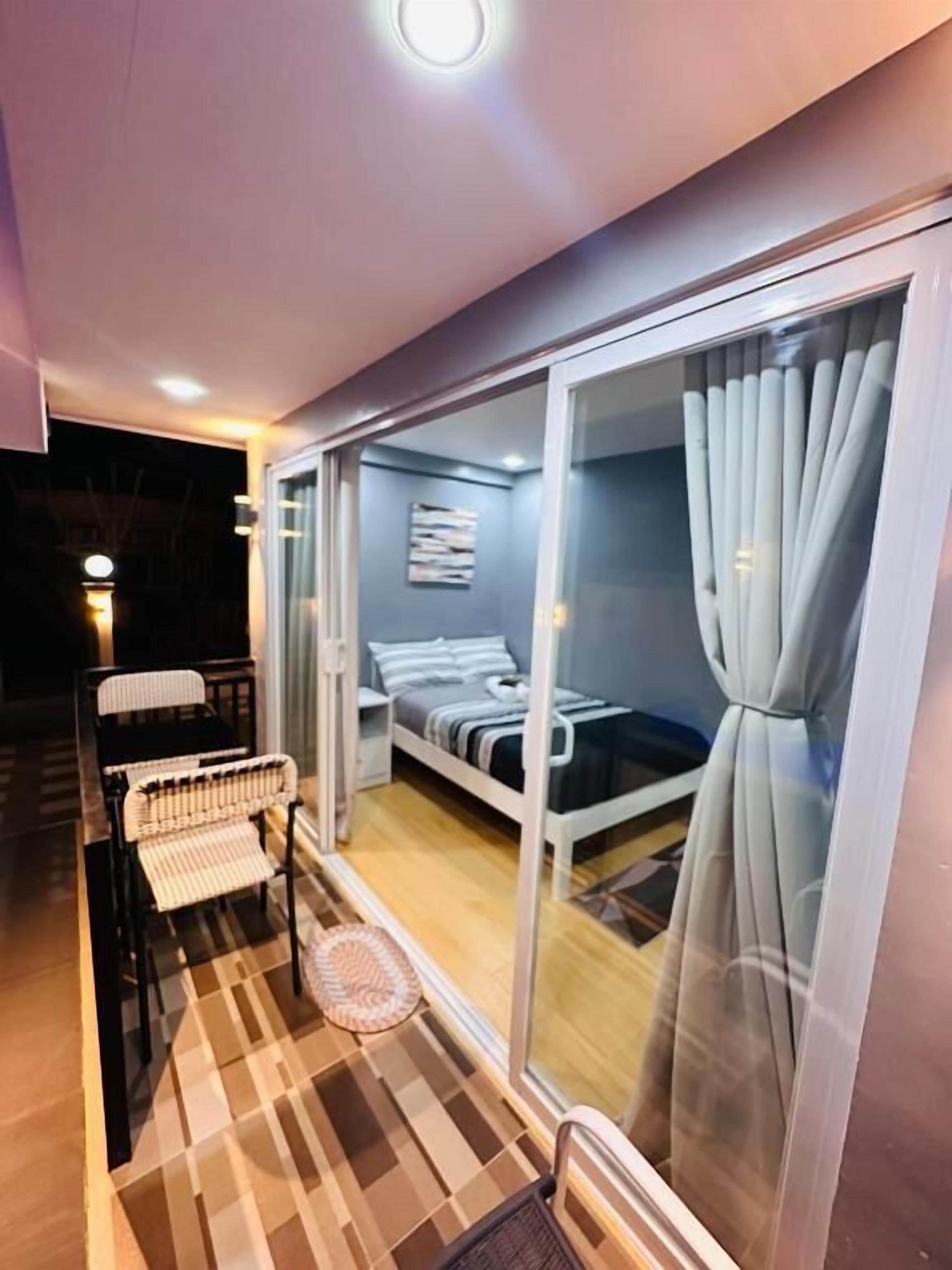 Quarto com cama, uma cadeira e uma pequena mesa. Porta de vidro deslizante dá acesso a uma área externa.
