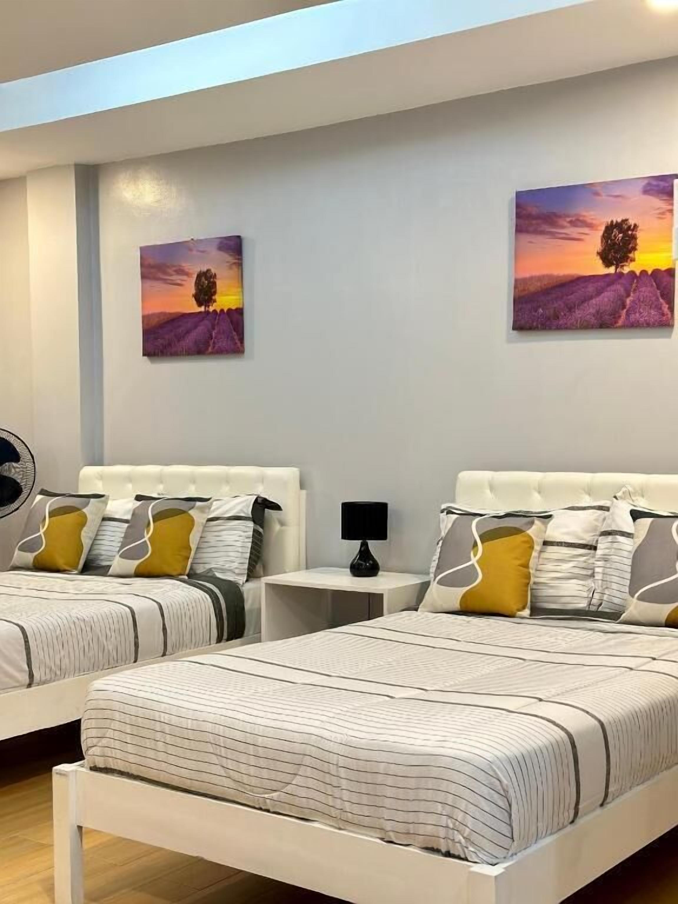 A hotel room with two beds, a nightstand, a lamp, and two paintings on the wall.