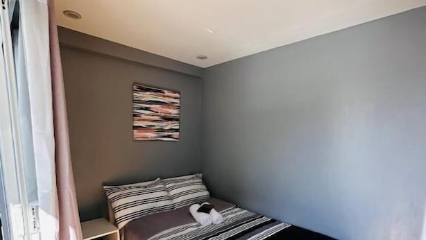 Un dormitorio con una cama, una mesita de noche, una obra de arte en la pared y una ventana con cortinas.