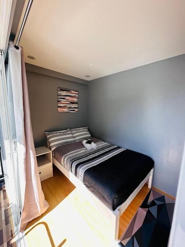 A bedroom with a bed, a nightstand, a wall-mounted artwork, and a window with curtains.