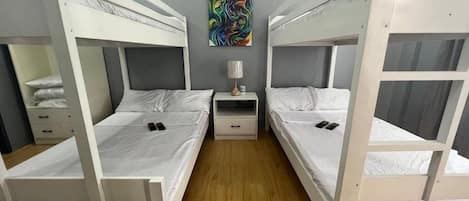 Una habitación con literas, una mesita de noche con lámpara y un cuadro en la pared.