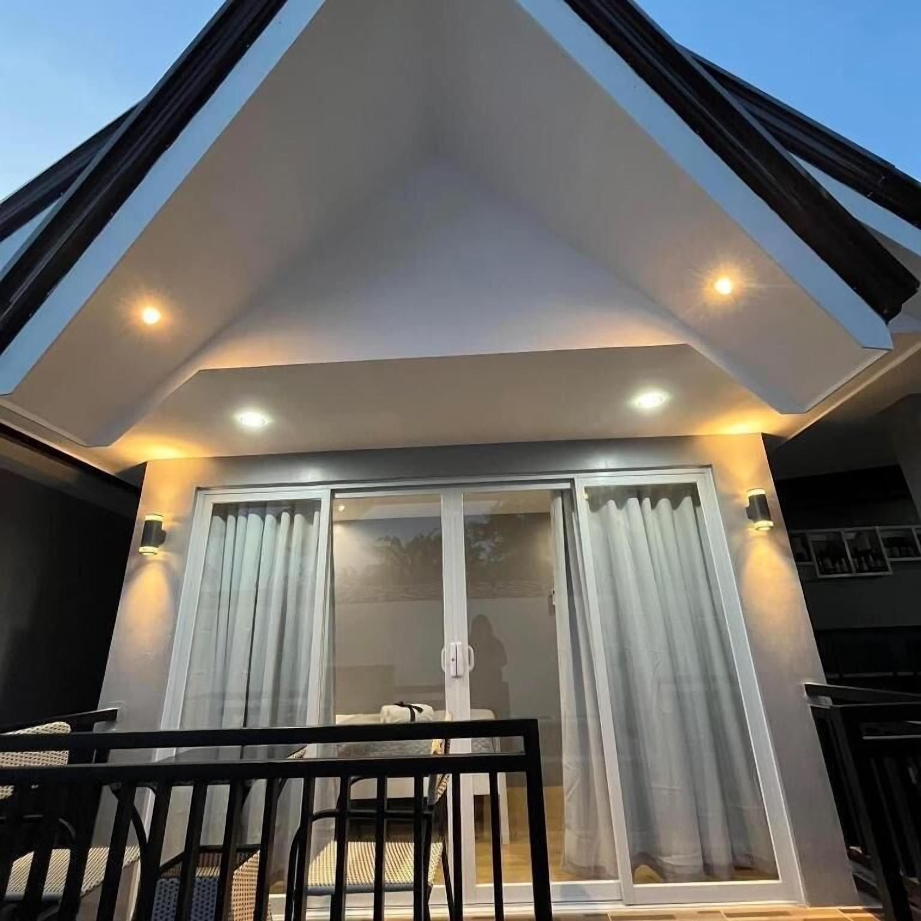 Um edifício moderno com área externa coberta, destacando uma entrada com porta de vidro e um espaço de estar com mesa e cadeiras.