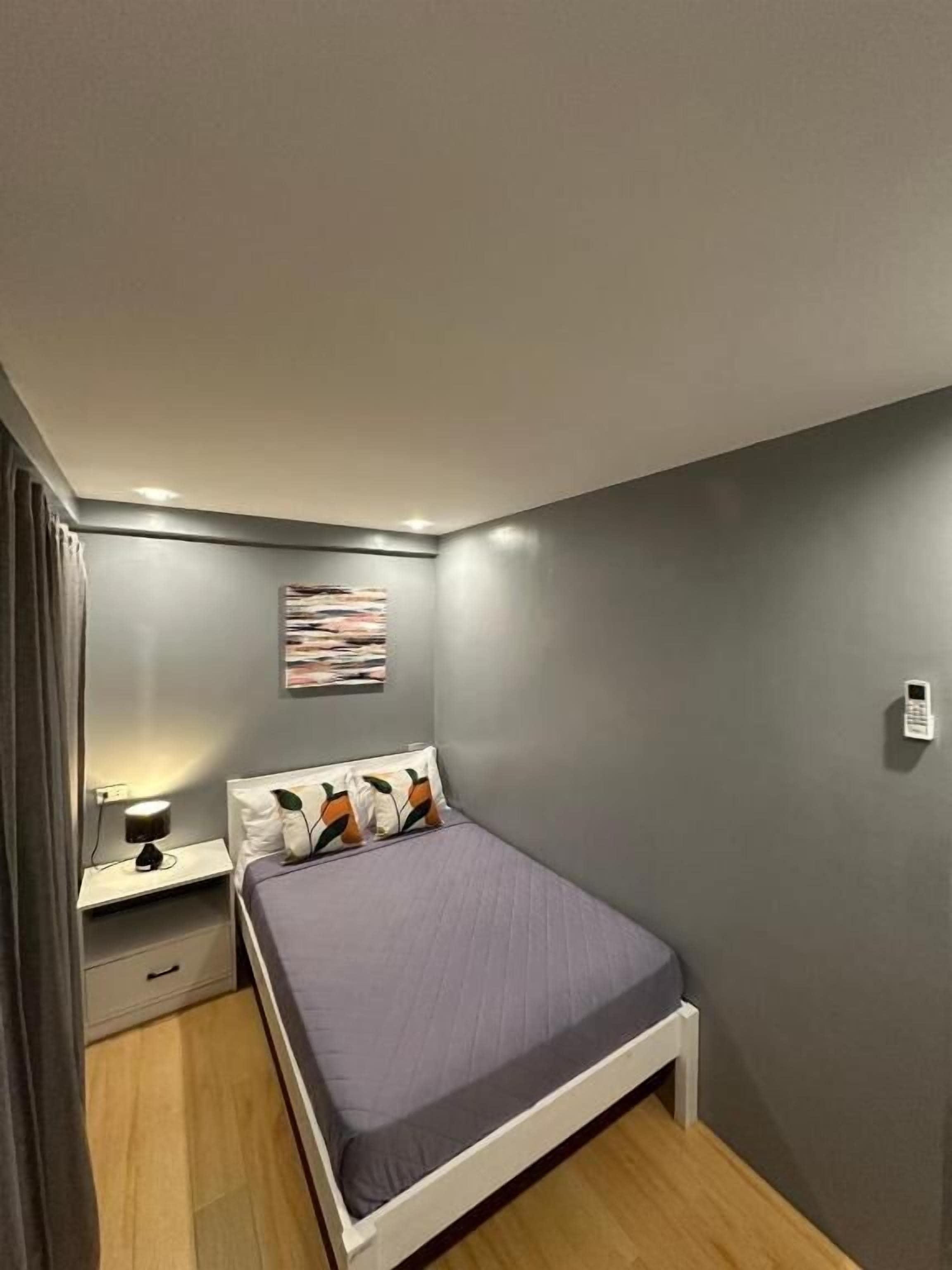 Un dormitorio con cama, mesita de noche, lámpara y teléfono en la pared.