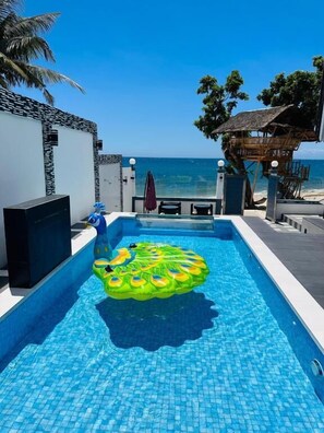 A pool with a floating ring, a palm tree, and a view of the ocean. - D' Beach Resort (Puerto Princesa)