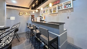 Una zona de bar con mostrador, taburetes y estanterías llenas de botellas y vasos.