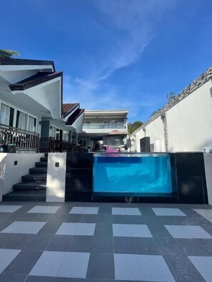 A modern residential property with a swimming pool, a staircase leading to a second floor, and a gated entrance.